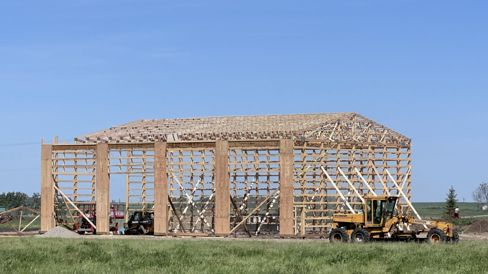 The BlackTop Enduro manufacturing building under construction near Strathmore, Alberta — wood post-frame framing against a blue prairie sky, with a grader on site